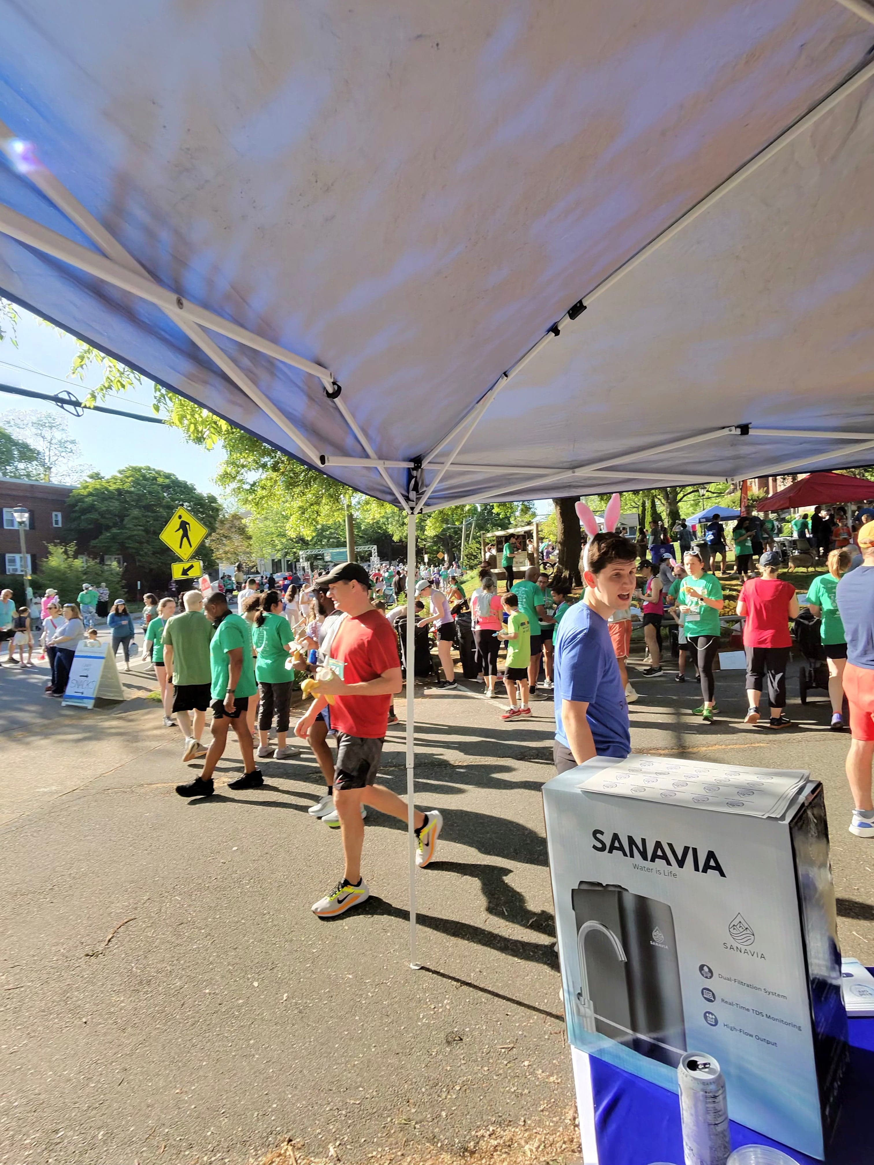 Sanavia's booth under a tent as runners pass by at the Arlington Bunny Hop 5K