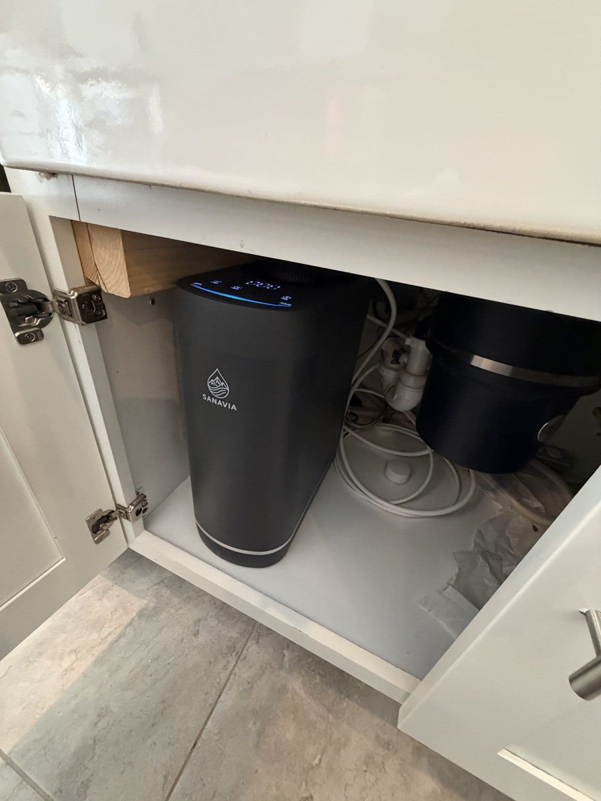 The Hydra installed under a white farmhouse sink, display lit, beside the garbage disposal